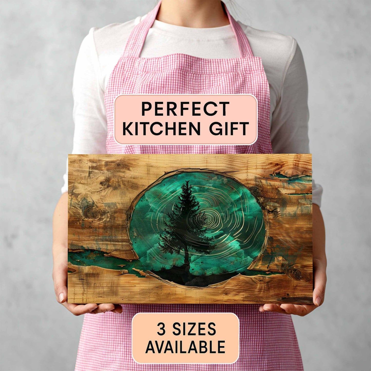 Person holding a tempered glass cutting board with a tree design, wearing a pink apron with text.
