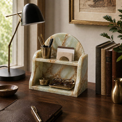 A marble desktop organizer with a light green and cream veined pattern, styled on a dark wooden desk next to a black desk lamp, books, and a plant.