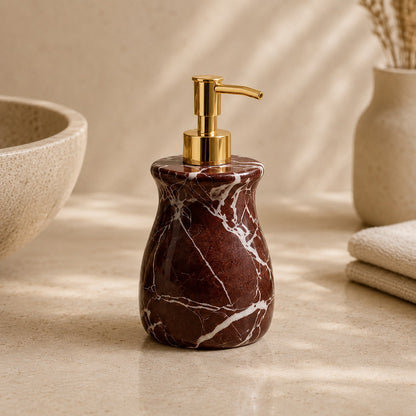 A dark brown marble soap dispenser with white veining and a polished gold pump, styled on a beige countertop with a ceramic bowl and folded towels in the background.