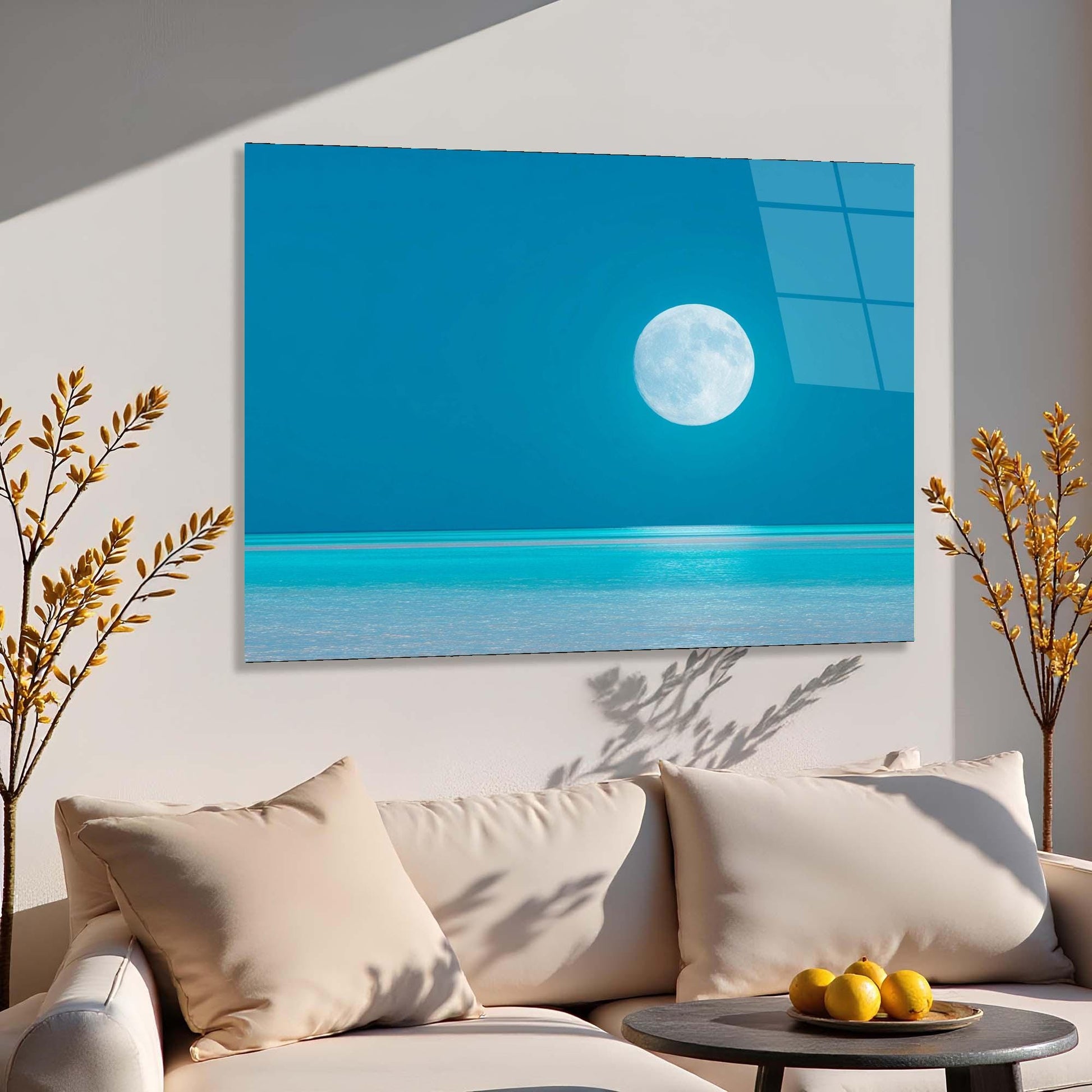 Sofa with decorative pillows and a small table with fruits, featuring a large wall art of a beach scene with a moon.