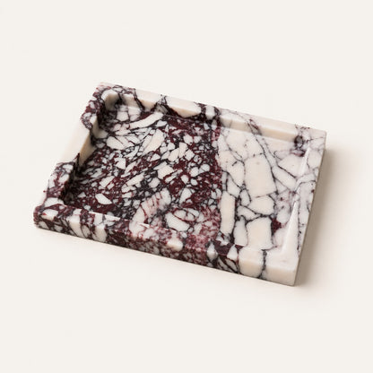 A rectangular marble tray with a raised rim, featuring a marbled pattern of white, deep burgundy, and black veining, photographed on a light cream background.
