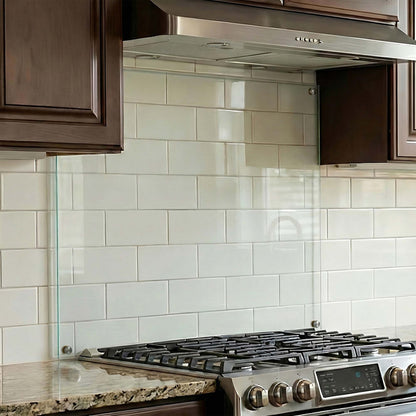 Stainless steel stove with clear glass backsplash in a kitchen setting