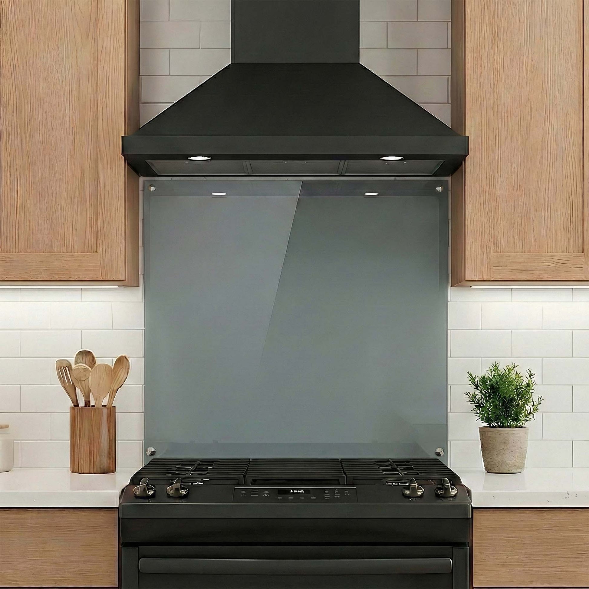 Black range hood, stove and glass backsplash in a kitchen with wooden cabinets and white tiles.