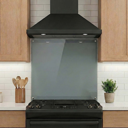 Black range hood, stove and glass backsplash in a kitchen with wooden cabinets and white tiles.