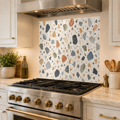 Grout-free terrazzo pattern tempered glass backsplash behind a kitchen sink with a matte black faucet.