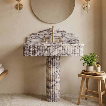 Calacatta viola marble pedestal sink in a bathroom setting with a stool and plant.