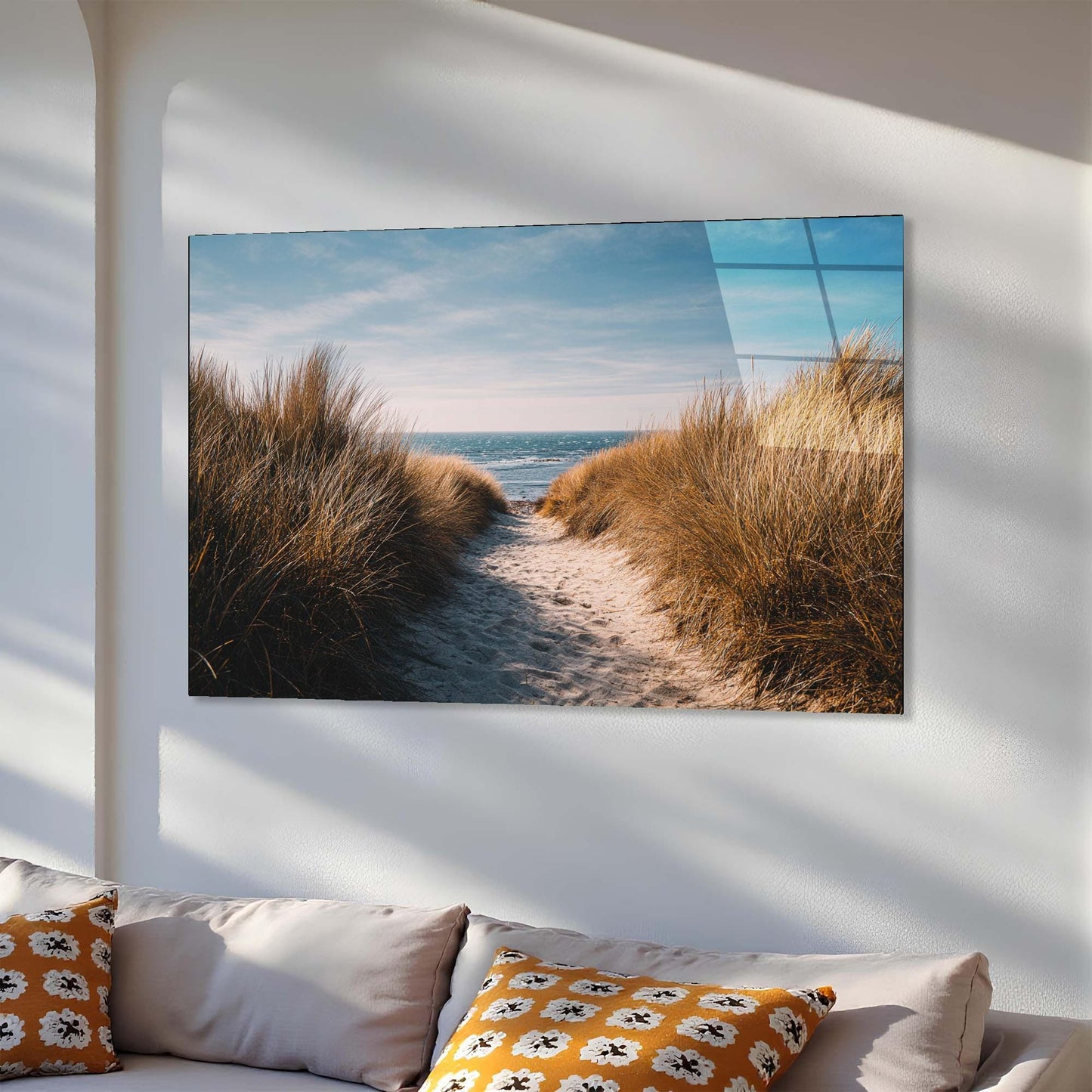 Wall art of a beach scene with sand and grass on a white wall above a sofa.