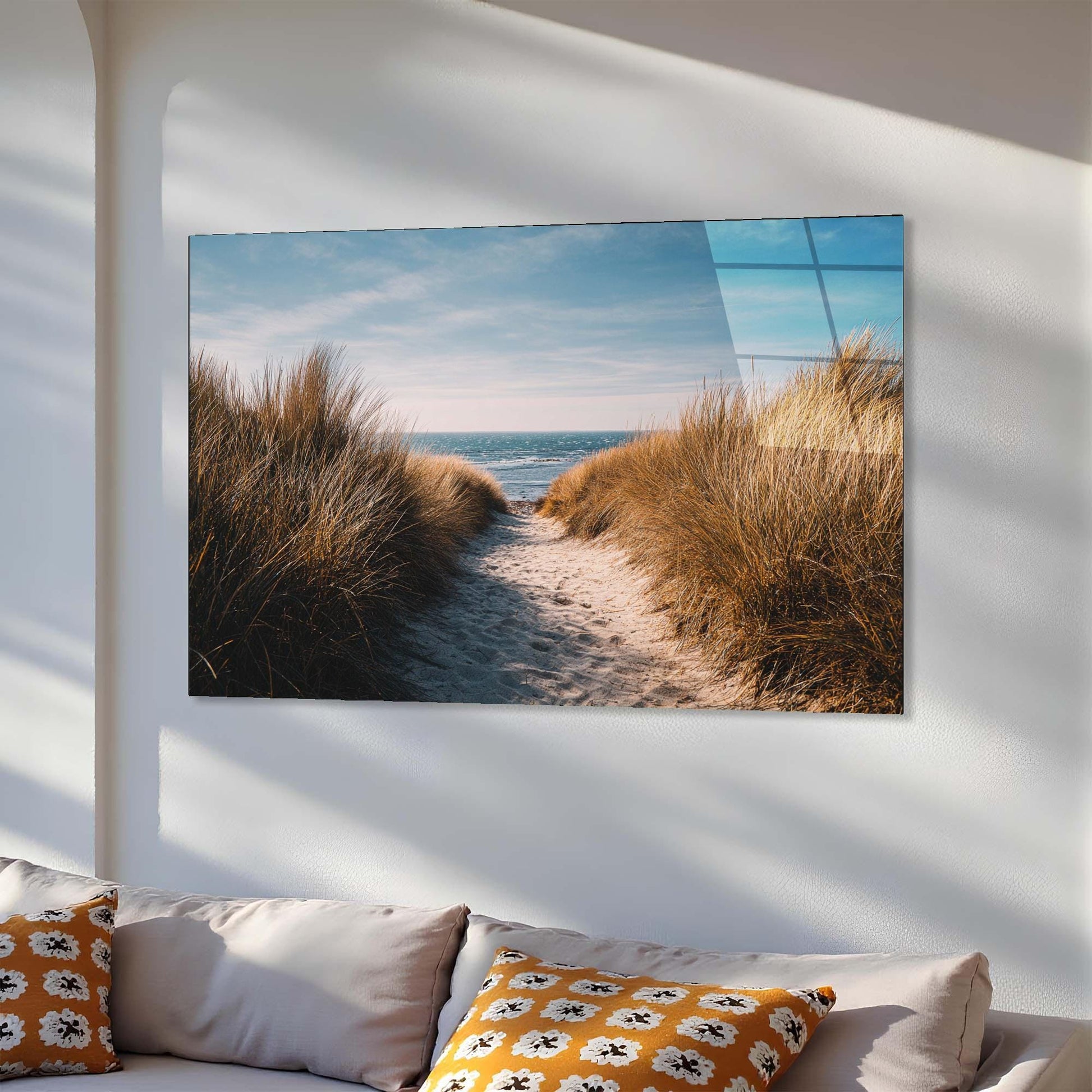 Wall art of a beach scene with sand and grass on a white wall above a sofa.