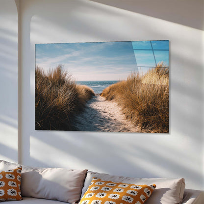 Wall art of a beach scene with sand and grass on a white wall above a sofa.