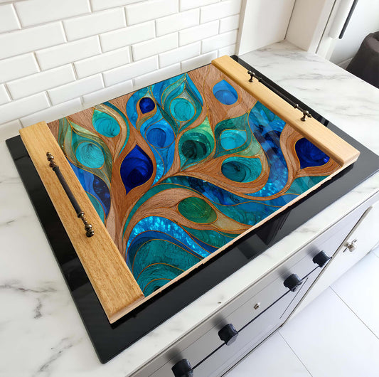 Decorative glass panel stove top cover with peacock feather design on a stove