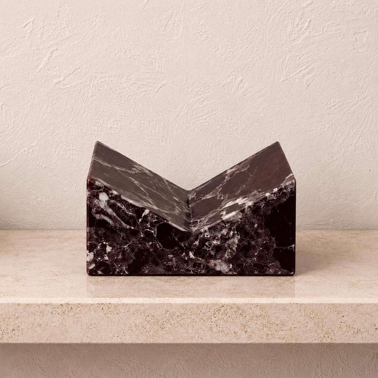 Rosso Levanto marble book stand with deep burgundy veining on a light shelf.