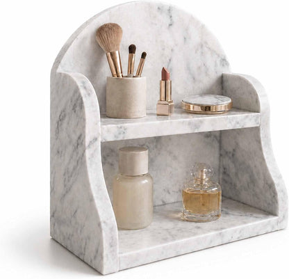 A white and gray marble vanity organizer with two shelves, styled with makeup brushes, a lipstick, a compact mirror, a cosmetic bottle, and a perfume bottle on a white background.