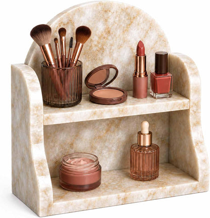 A marble-look cosmetic organizer with two shelves and a rounded backrest, styled with makeup items including brushes, lipstick, powder, and bottles on a white background.