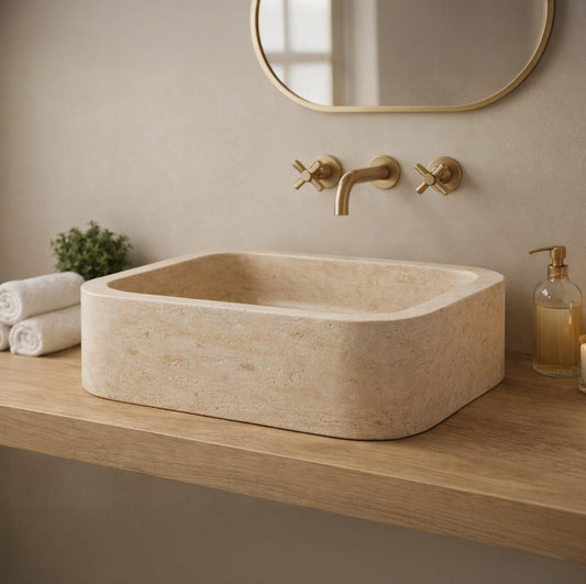 Beige stone sink with gold faucet and mirror in a bathroom setting