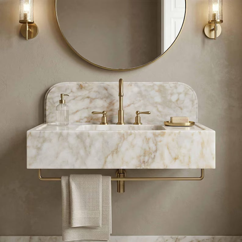 Bathroom vanity with marble countertop, gold fixtures, and round mirror.