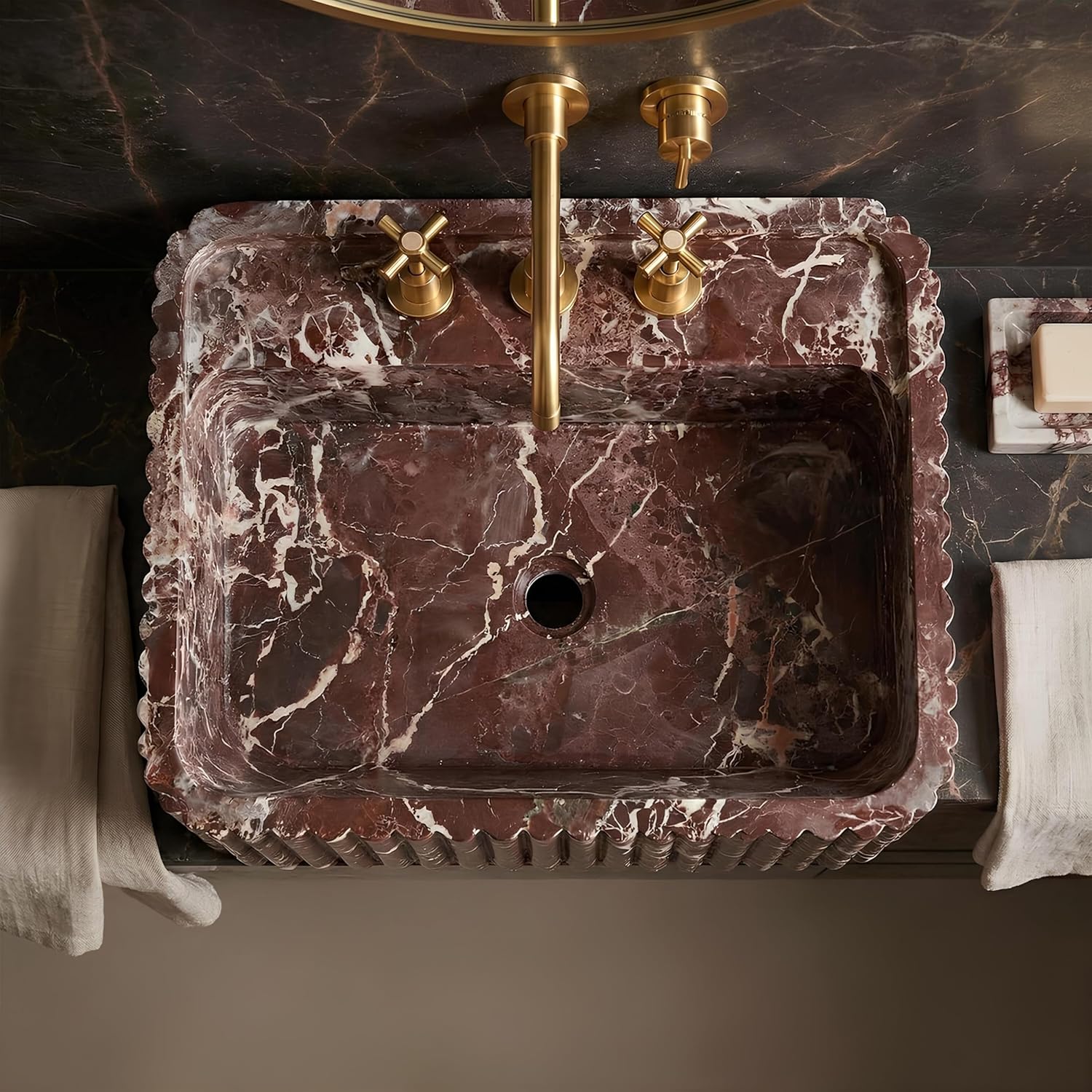 Marble sink with gold faucet and handles on a dark marble wall.