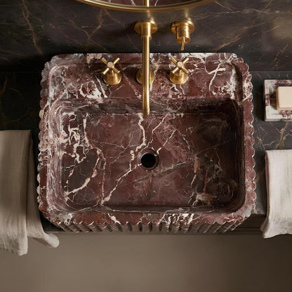 Marble sink with gold faucet and handles on a dark marble wall.