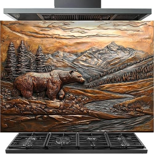 A stainless steel range hood with a decorative wall panel featuring a detailed 3D-style relief sculpture of a brown bear in a mountain landscape with trees and a river, shown above a black gas range.