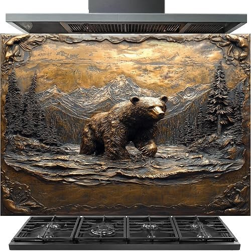 A large stainless steel range hood with a decorative bronze-finished front panel featuring a detailed relief sculpture of a bear in a mountain forest landscape. A black gas cooktop is visible beneath the hood.