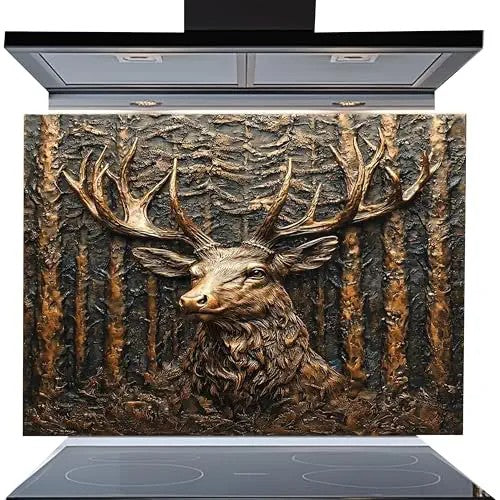 A decorative kitchen backsplash panel featuring a highly detailed, textured 3D-style relief of a stag deer head with large antlers in front of a forest background. The panel is shown installed on a modern black induction cooktop with a matching black range hood above, set against a plain white background.