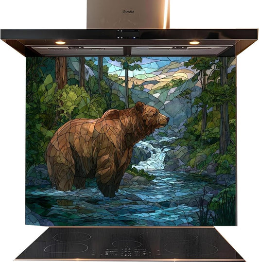 A kitchen backsplash panel featuring a stained-glass-style illustration of a brown grizzly bear standing in a blue stream surrounded by green trees and mountains. The panel is installed on a black induction range hood and cooktop against a white background.
