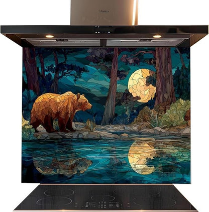 A kitchen range hood with a large decorative glass splashback panel featuring a stylized bear, moon, trees, and water reflection in blue, teal, brown, and gold tones. The hood itself is black with built-in lights, shown above a black induction cooktop on a white background.