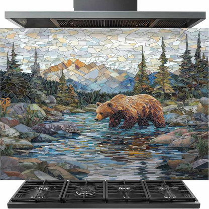 A stainless steel gas range hood with a large mosaic tile backsplash depicting a brown bear walking through a rocky stream with mountains and pine trees in the background, shown above a black gas cooktop.