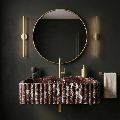 Bathroom vanity with marbled sink, round mirror, and gold fixtures on a dark wall.